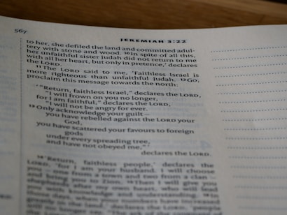 A close-up view of an open book showing text from the Bible, specifically Jeremiah 3:22, with printed lines and numbers visible on a slightly curved page.