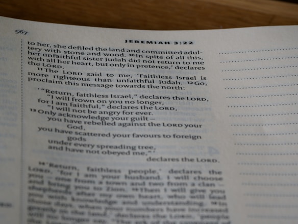 A close-up view of an open book showing text from the Bible, specifically Jeremiah 3:22, with printed lines and numbers visible on a slightly curved page.