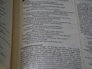 A close-up view of an open book displaying text written in a poetic format across two pages. The left page focuses on verse-style text with religious language, possibly from a scripture. The right page has more formal prose, with headings such as 'Unfaithful Israel'. The pages are cream-colored with dark text and a faint blue tint.