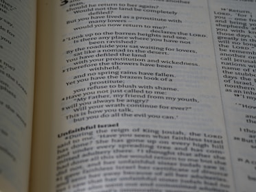 A close-up view of an open book displaying text written in a poetic format across two pages. The left page focuses on verse-style text with religious language, possibly from a scripture. The right page has more formal prose, with headings such as 'Unfaithful Israel'. The pages are cream-colored with dark text and a faint blue tint.