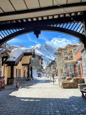 The Village at Palisades Tahoe base plaza with snow on the roofs and a snowy granite peak filling the gap between the buildings