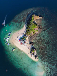 A panoramic view of a small island with white sandy shores and boats anchored nearby.