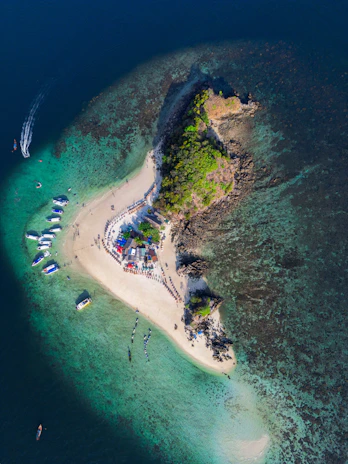 A panoramic view of a small island with white sandy shores and boats anchored nearby.