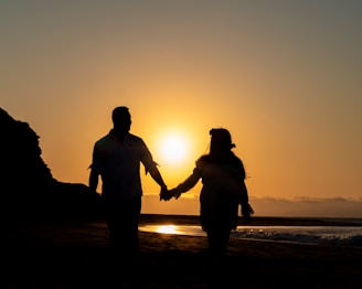 a man and a woman hold hands as the sun sets