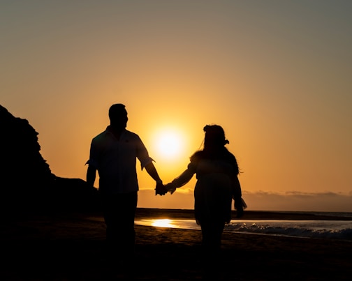a man and a woman hold hands as the sun sets