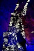 Black and white image of soldiers appears projected onto rough, rocky cave walls, creating a historical and ghostly effect. The distinct contrast between the monochrome figures and the vibrant blue and purple lighting surrounding them creates a surreal, immersive environment.