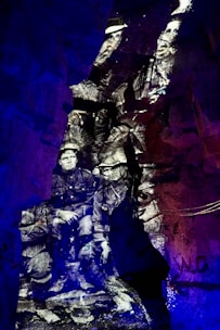 Black and white image of soldiers appears projected onto rough, rocky cave walls, creating a historical and ghostly effect. The distinct contrast between the monochrome figures and the vibrant blue and purple lighting surrounding them creates a surreal, immersive environment.