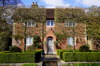 A charming two-story brick home with a well-manicured front yard and large windows letting in natural light.