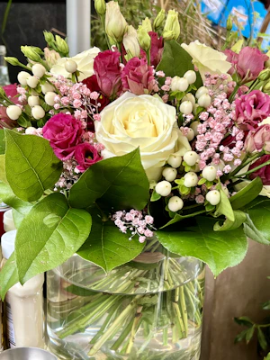 A vibrant bouquet of mixed seasonal flowers in soft pink and white tones, artfully arranged in a clear glass vase.