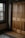 A wooden wardrobe with paneled doors is adjacent to a window with dark wooden frames. The interior is warmly lit, highlighting the natural grain of the wood. A patterned rug lies on the wooden floor.