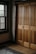 A wooden wardrobe with paneled doors is adjacent to a window with dark wooden frames. The interior is warmly lit, highlighting the natural grain of the wood. A patterned rug lies on the wooden floor.