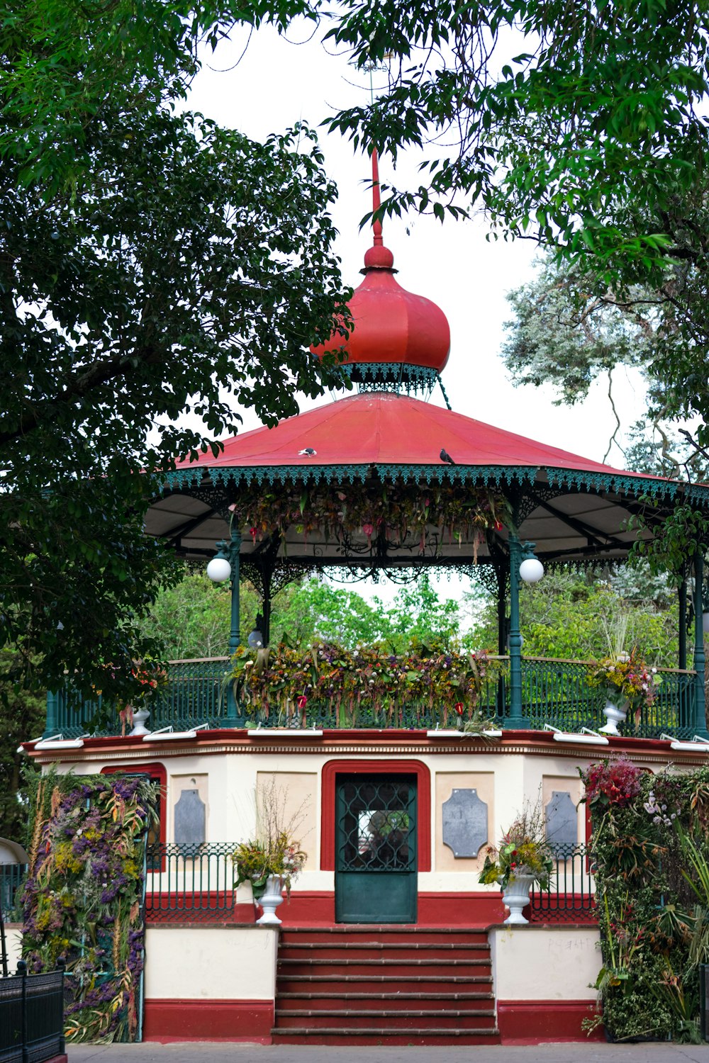 a gazebo with a red roof surrounded by greenery