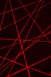 Red laser beams crisscross against a dark background, creating an intricate web of intersecting lines.