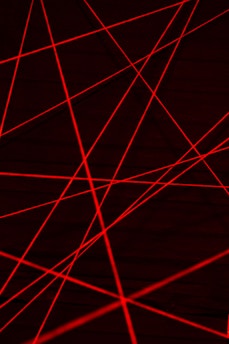 Red laser beams crisscross against a dark background, creating an intricate web of intersecting lines.