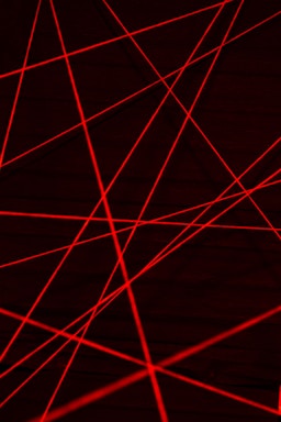 Red laser beams crisscross against a dark background, creating an intricate web of intersecting lines.