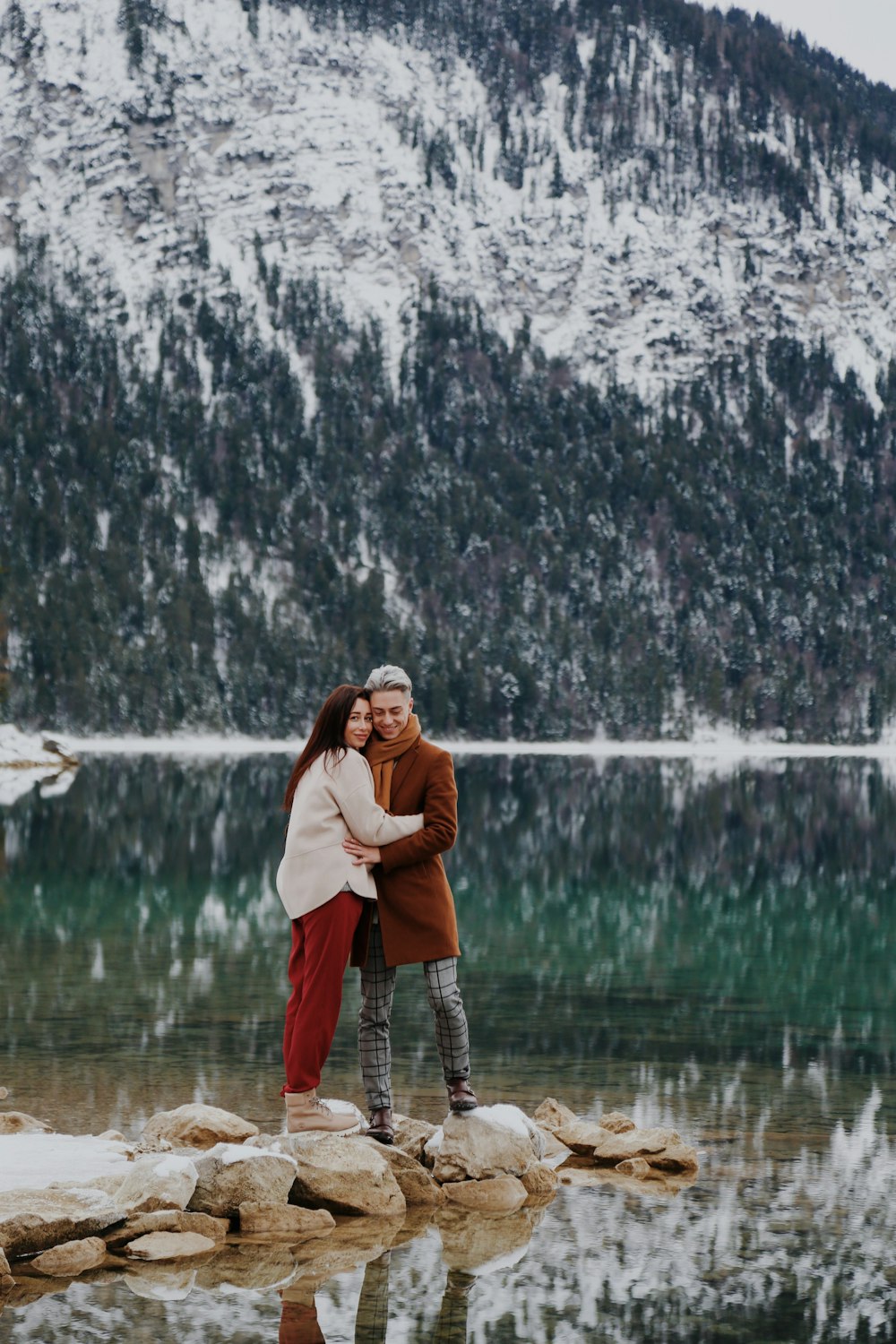 a man and a woman standing on rocks near a lake