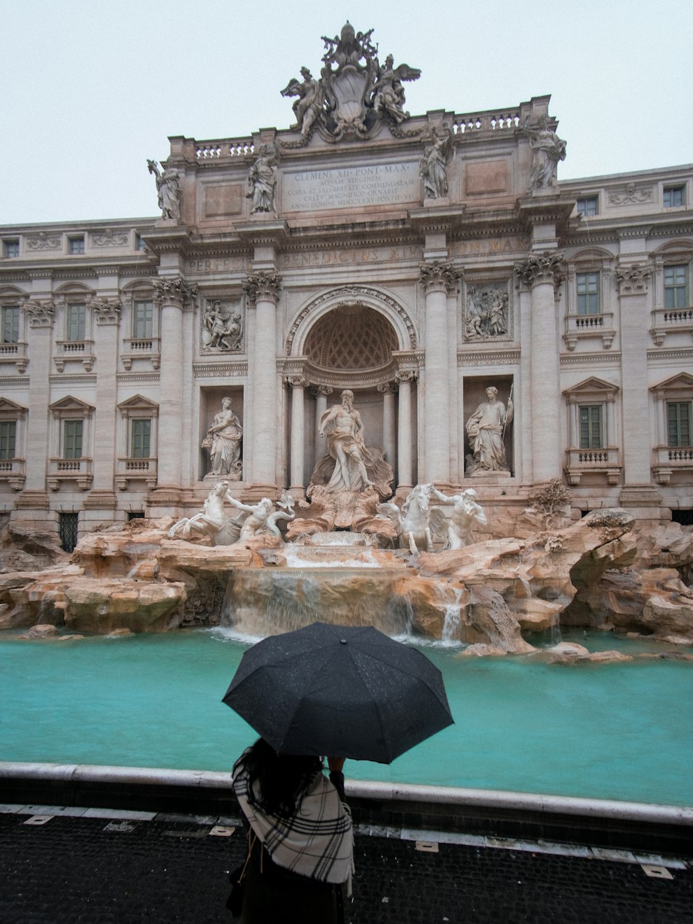 a person with an umbrella standing in front of a fountain