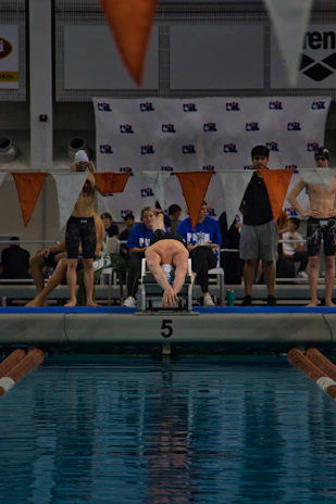 Young swimmers diving into the pool at the start of a race under bright indoor lights