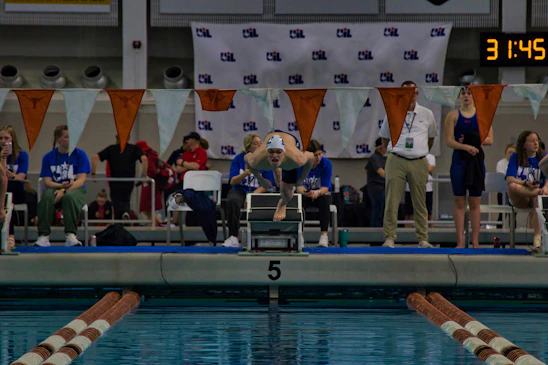 A group of CNCA swimming officials attentively observing a swim meet, clipboard in hand, by the poolside.