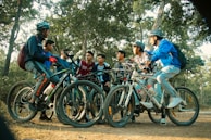 Teenagers laughing and biking together on a tree-lined trail during golden hour.