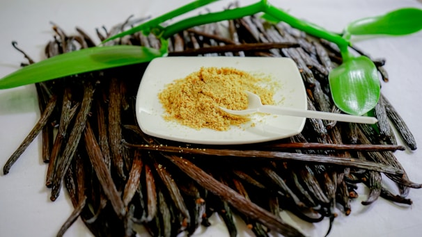 Close-up of a spoonful of fine white stevia powder on a rustic wooden table with green stevia leaves nearby.