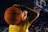 A young person is holding a basketball in front of a large crowd in a sports arena. They are wearing a yellow jersey with green trim, which has text on it, and are smiling confidently.
