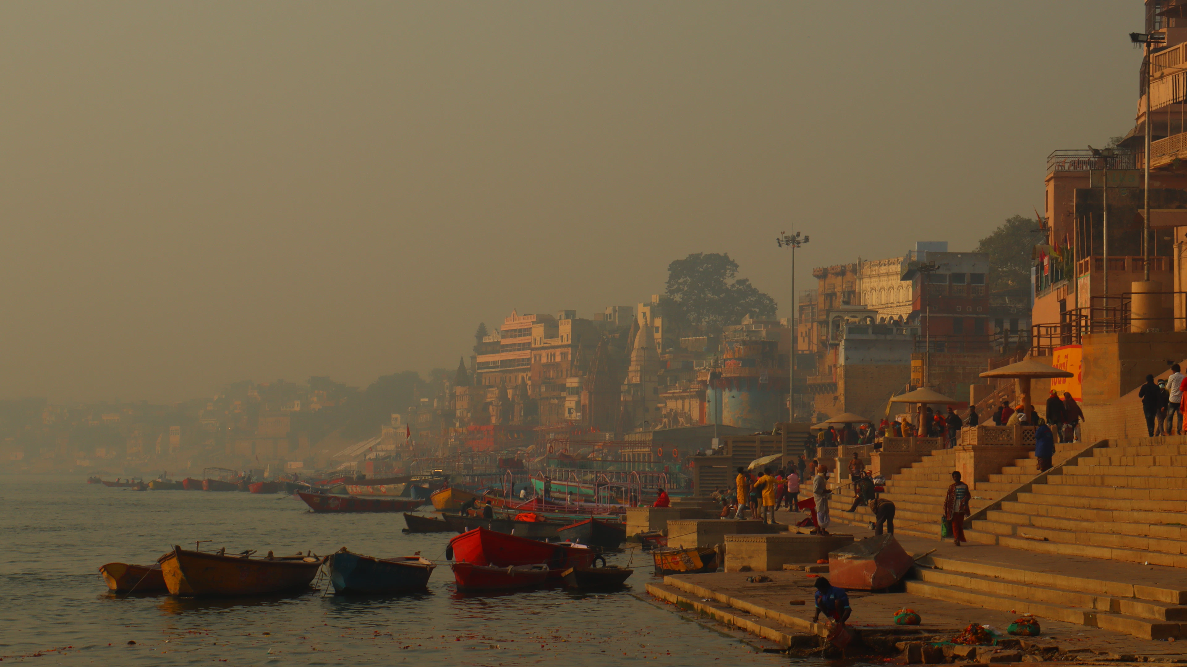 The ghats at Varanasi in morning mist, boats moored along the steps and figures moving on the stone