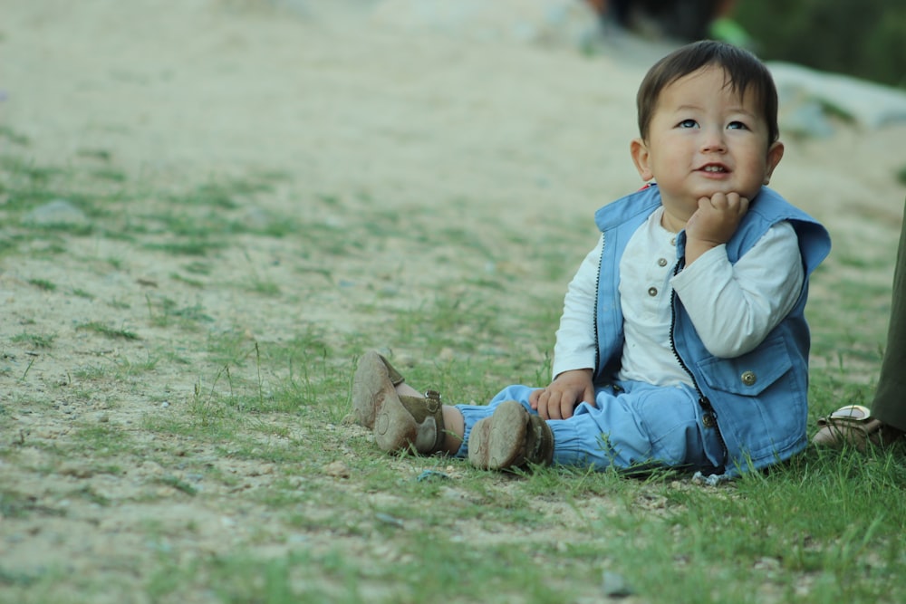 a little boy sitting on the ground in the grass