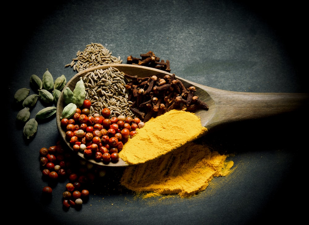 a wooden spoon filled with different types of spices