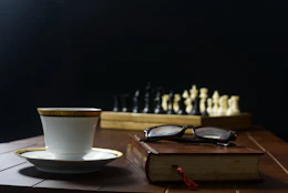 a cup of coffee next to a book and a chess set