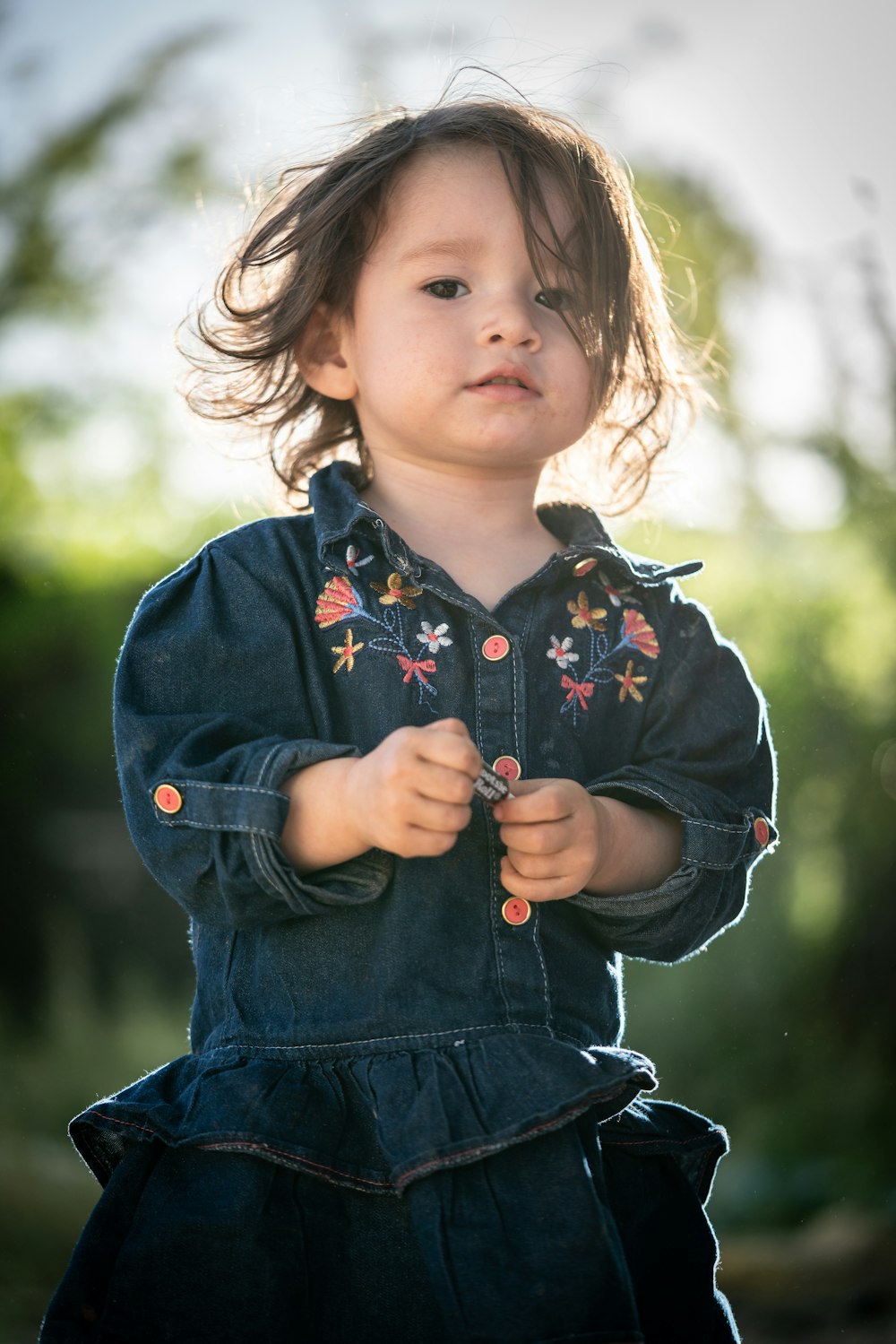 a little girl in a denim dress standing in a field