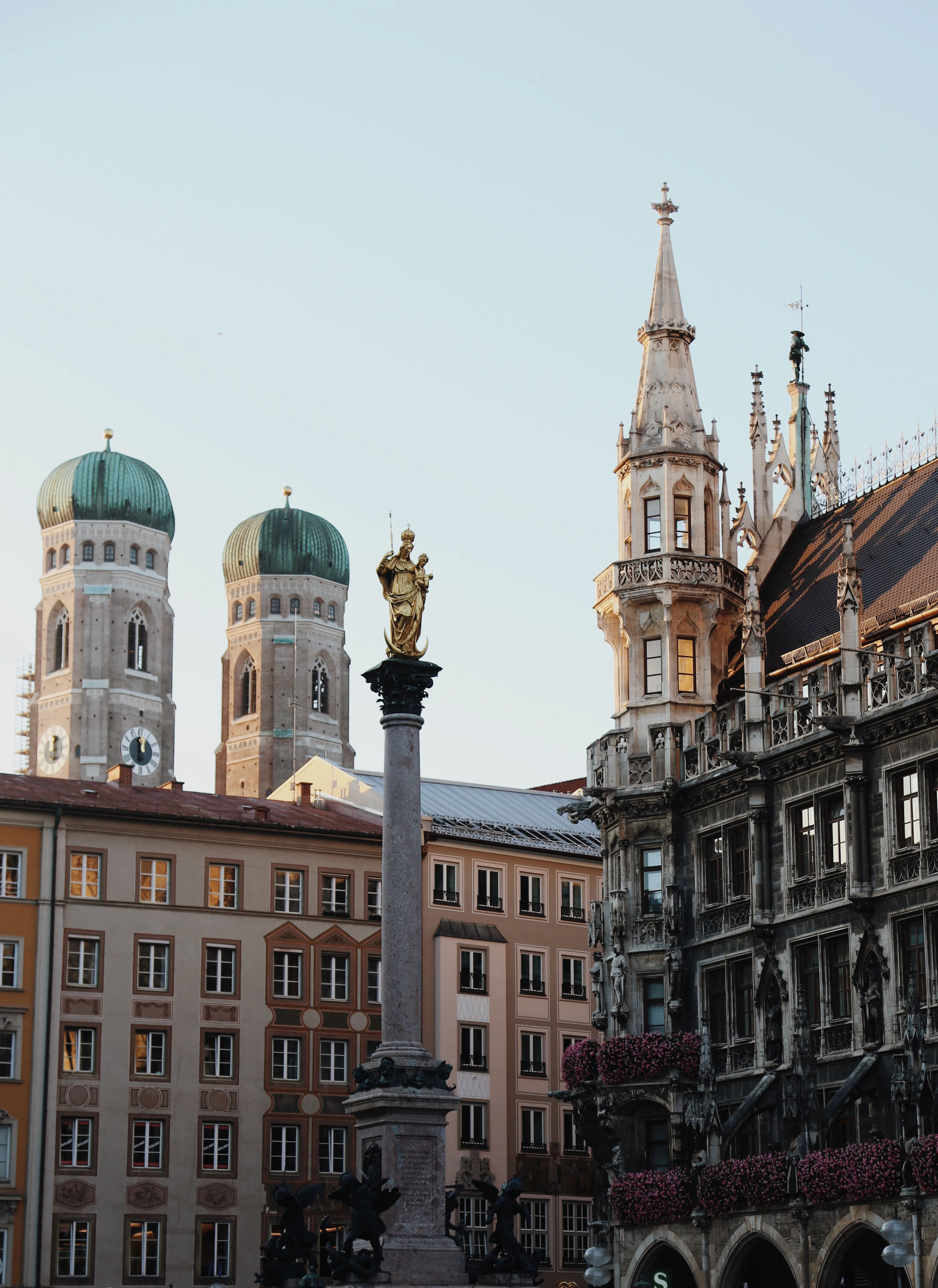 The golden Virgin Mary atop the Mariensaule column on Marienplatz in Munich, with the twin green onion domes of the Frauenkirche behind and the New Town Hall's spire to the right.