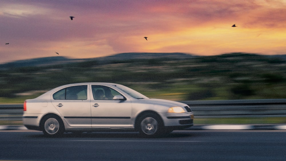 a white car driving down a road next to a forest