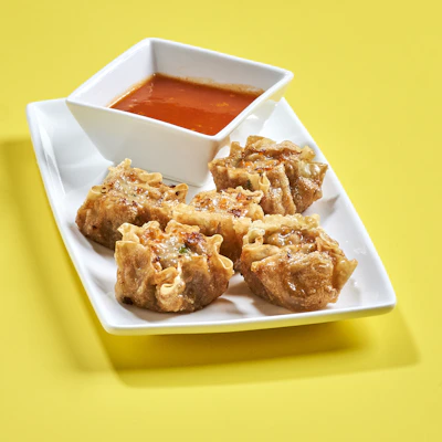A close-up of a vibrant plate featuring golden fried dumplings with dipping sauce.