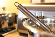 A stainless steel whisk and wooden spoon crossing each other in a ceramic utensil holder.