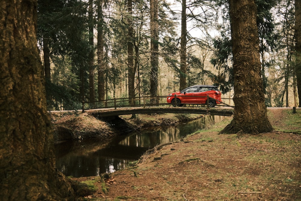 a red car driving across a bridge in the woods