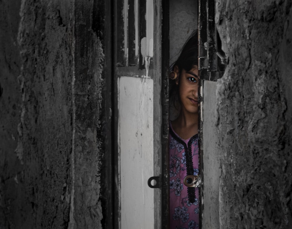 a young girl peeks out of a hole in a wall
