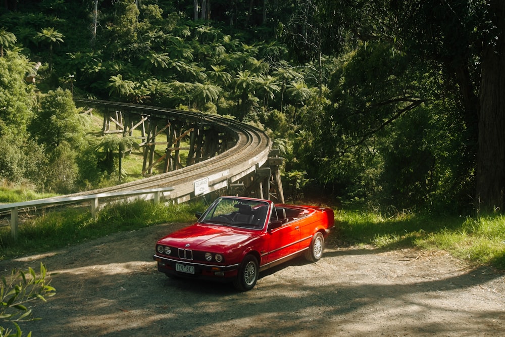 a red car parked on a dirt road next to a forest