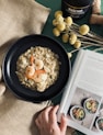 a person reading a book next to a bowl of oatmeal