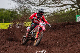 Rider wearing bold red and black motocross gear speeding through dirt track.