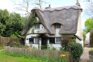 a white house with a thatched roof and a wooden fence