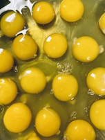 Multiple egg yolks floating in viscous egg whites, with bubbles and reflections of light creating a shiny surface.