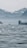 A serene landscape featuring a calm body of water with gentle ripples. In the background, there are misty mountains and a hazy sky, creating a tranquil and peaceful environment. The scene captures the quiet beauty of nature.