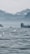 A serene landscape featuring a calm body of water with gentle ripples. In the background, there are misty mountains and a hazy sky, creating a tranquil and peaceful environment. The scene captures the quiet beauty of nature.