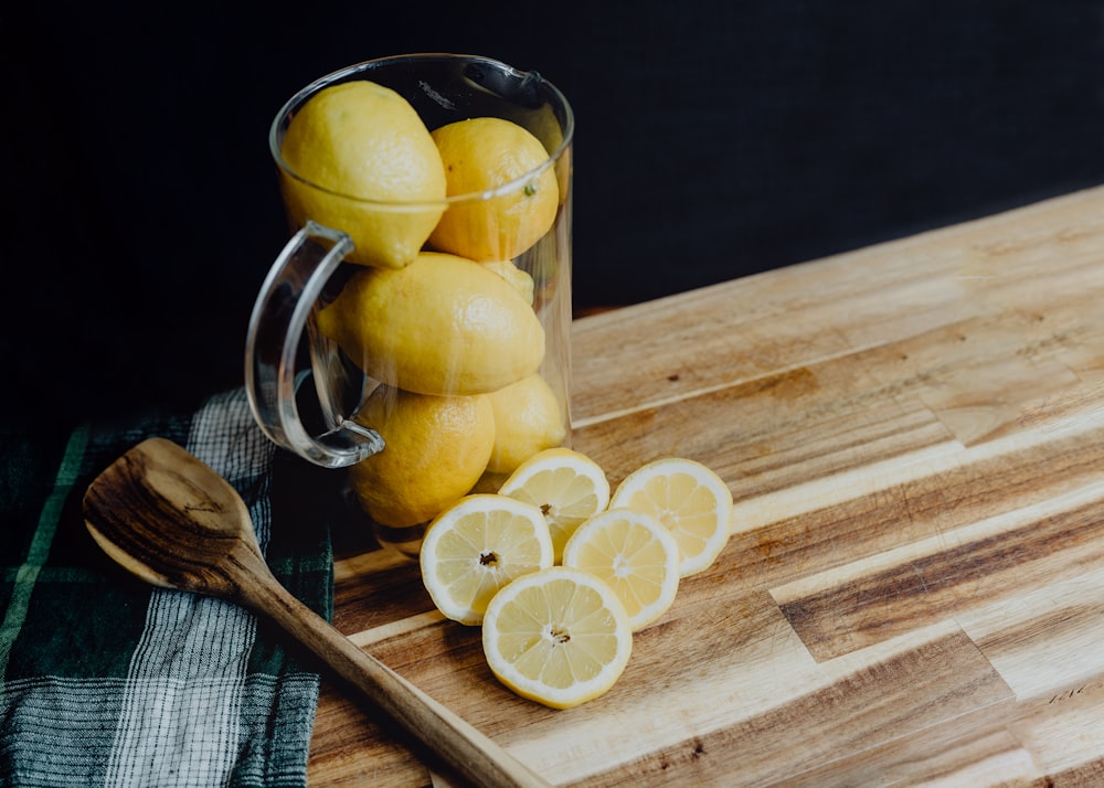 a pitcher filled with lemons on top of a wooden cutting board