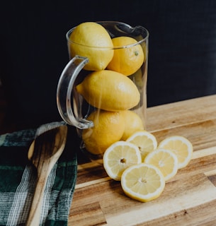 Close-up of freshly squeezed lemons dripping vibrant juice into a glass pitcher.