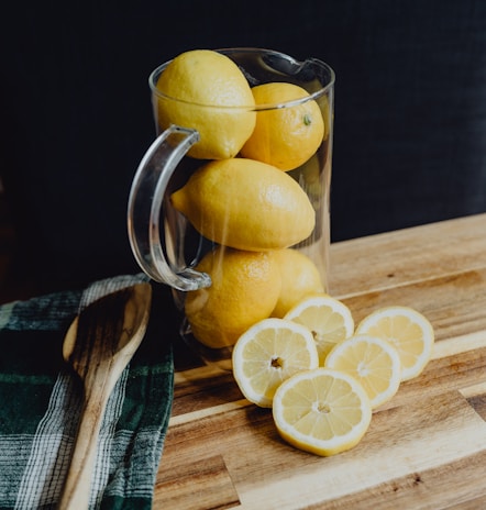 Close-up of freshly squeezed lemons dripping vibrant juice into a glass pitcher.