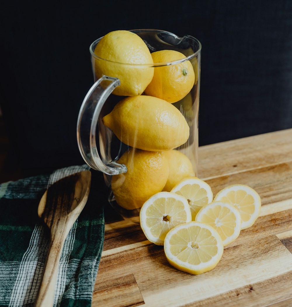 a glass mug filled with lemons on top of a wooden cutting board