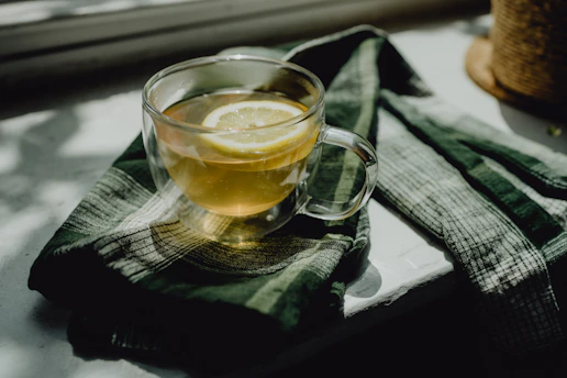 A vibrant glass of lemon tea beside a plate of assorted snacks in a cozy cafe setting.