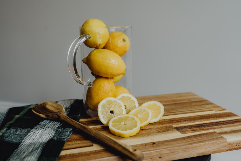 a glass pitcher filled with lemons on top of a cutting board